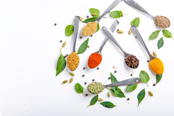 Various spices ( cumin, coriander, curry, paprika, chili, turmeric cinnamon, fenugreek, cardamom, basil leaf, parsley, cloves )  in  spoons on white background. Top view with copy space.