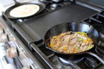 Mexican style pulled pork, known as carnitas, cooking in a cast iron skillet with a flour tortilla on a camal skillet.