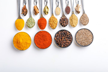 Various spices ( cumin, coriander, curry, paprika, chili, turmeric cinnamon, fenugreek, cardamom, basil leaf, parsley, cloves )  in  spoons on white background. Top view with copy space.