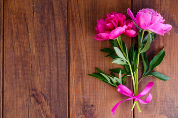Two beautiful peonies with ribbon on wooden table