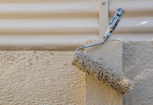 A used paint roller hangs on a wall to dry out image in landscape format with copy space