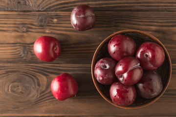 Fototapeta na wymiar Bowl of plums and three plums on a wooden table. Flat lay.