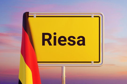 Riesa. Gelbes Schild/Ortsschild. Flagge von Deutschland h&auml;ngt dar&uuml;ber. Himmel mit Sonnenuntergang oder Sonnenaufgang