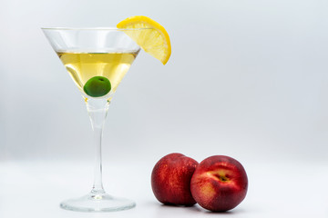 Martini with olive in glass. Peaches next to martini on a white background. A slice of lemon as a decoration for a drink. 