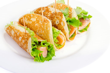 Snack rolls from pancakes, salmon and green salad leaves. 