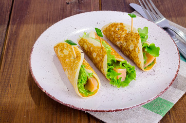 Snack rolls from pancakes, salmon and green salad leaves. 