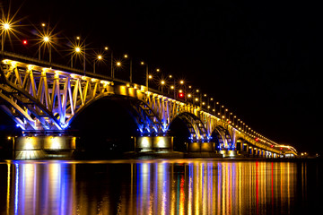 Saratov night bridge in bright lights from the light of lanterns and long highlights on the water