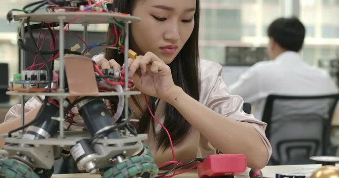 Asian female electronics engineer works with robot, building, fixing robotics in workshop. People with technology or innovation concept.