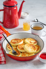 Cottage cheese pancakes  in a red frying pan on a marble background. Syrniki with  strawberry sauce and honey for breakfast. Selective focus