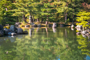 Charming corner of the Japanese Zen Gardens in autumn with rocks, lanterns and reflections in the pond at the Golden Pavilion in Kyoto, Japan.