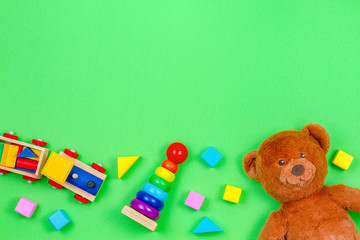 Baby kids toys background frame with teddy bear, wooden toy train, baby stacking rings pyramid and colorful blocks on green background