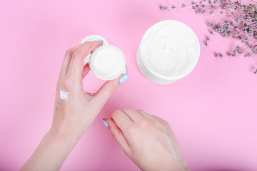 Hand care. Woman holding cream tube and applying moisturizer cream on her beautiful hands for soft hand skin on pink pastel background. Top view, minimalism, flat lay.