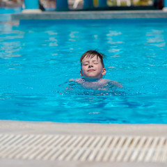 Learning to swim. Boy swimming along the side of pool.