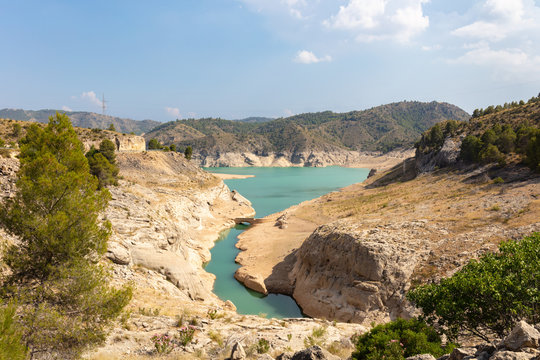 The large reservoir Fuensanta near Albacete in Spain. The water is turquoise green. Low water level. An old street and bridge is visible. Sunshine and blue sky.