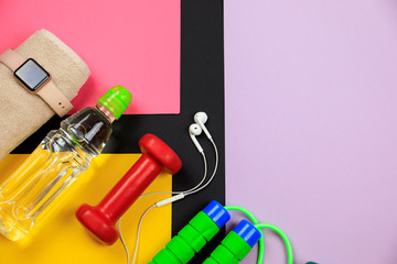 Fototapeta na wymiar Sports equipment for fitness training on a color background. Bottle with water, smart watch, earphones and jumping-rope. Set for sports activities.