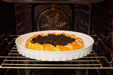 Freshly made homemade galette with black raspberries and apricot in the domestic oven. Shallow focus.