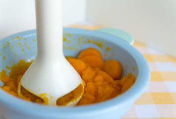 Chopping and mixing boiled or stewed carrots in a bowl with mixer. Preparing baby food, homemade. Healthy food kids concept. Selective focus.
