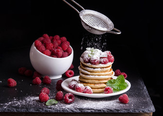 Bowl and  Pancakes with raspberries around on black backgound