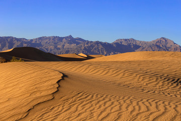 Sand dunes in a desert landscape in Death Valley California.  The vast barren land is dry and arid due to droughts result of global warming and climate change.