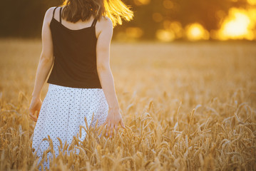 Photo of beautiful woman walking in wheat field at sunset