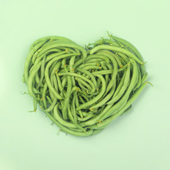 Heart of green beans on green background,  top view.