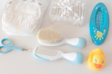 Baby essentials for hygiene concept: diapers, cotton swabs, scissors, hair comb, brush, thermometer, yellow rubber duck - top view