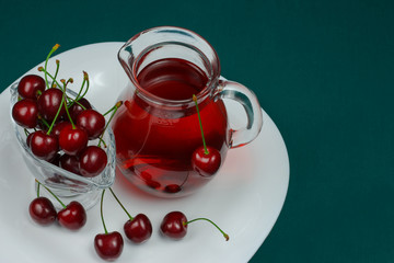 Cherry juice in a carafe on a white plate on a green background.