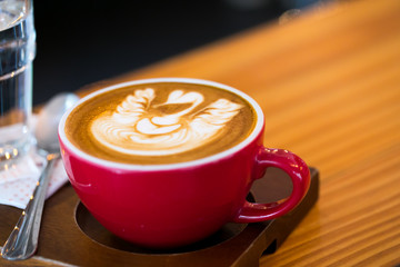 Red cups of hot Late coffee with froth swan shaped on table at coffee shop