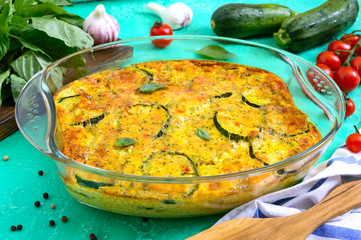 Zucchini, cheese, eggs, cream and green casserole in a transparent glass form on a bright background. Tasty healthy dish.