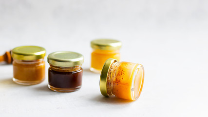 Four Small glass jar with metal cap with different kinds and colours of honey put in line and wooden spoon isolate and on grey cement background with copy space. Healthy product, natural. Horizontal
