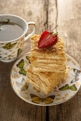Napoleon cake dessert decorated with strawberries on a beautiful plate with a cup of tea on an old wooden background