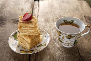 Napoleon cake dessert decorated with strawberries on a beautiful plate with a cup of tea on an old wooden background