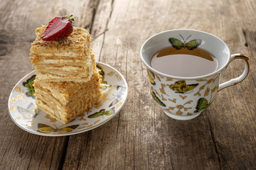 Napoleon cake dessert decorated with strawberries on a beautiful plate with a cup of tea on an old wooden background