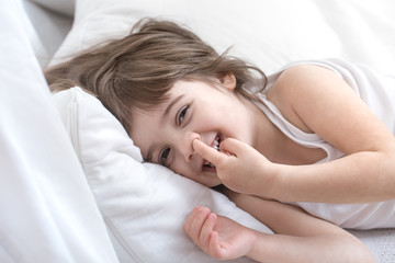Fototapeta na wymiar Cute little girl smiling while lying in a cozy white bed