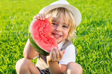 Little boy with watermelon sitting on the grass