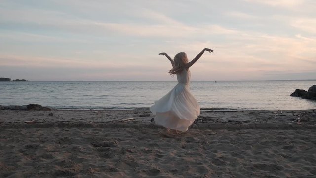 ballet dancer in a flowing dress dancing by the sea at sunset.