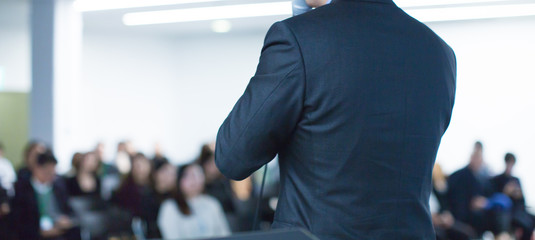 Speaker at conference giving a talk about corporate business. Audience in hall with presenter...