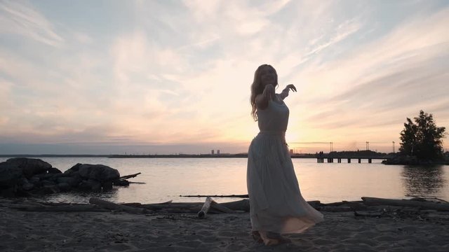 girl in a flowing dress dancing by the sea at sunset.