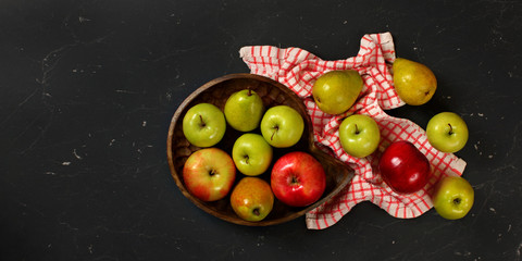 Tabletop view, wooden carved bowl with apples and pears, tablecloth, on black marble like board, space for text on left side