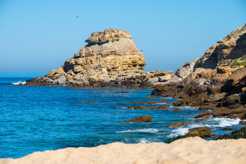 Fototapeta na wymiar Stones and rocks on a beach under sky blue Atlantic Ocean against the cliffs during sunny day
