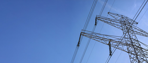 Looking up steel power pylon construction with high voltage cables against blue sky. Wide banner for electric energy industry with space for text on left side