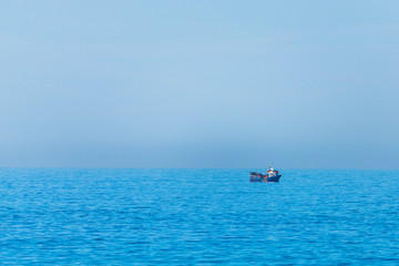 Minimalistic image of the sea with a fishing boat. Blue sea water and clear sky.