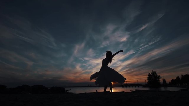 girl in a flowing dress. silhouette of a ballerina dancing at sunset near the water.