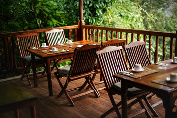 Empty wooden chairs and tables, with coffee cups upside down - ready for morning breakfast, jungle...