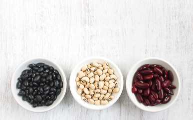 Assortment of beans in white bowl on rustic wood.