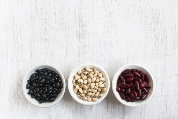 Assortment of beans in white bowl on rustic wood.