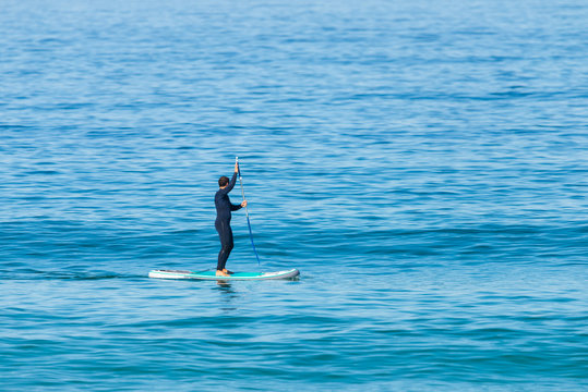 Stand up paddle boarder in wetsuit paddling on a sea. Minimalist image