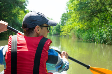 man is paddling on kayak on the river duct, green forest around