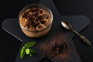 Mokachchino dessert in a jar on a black stone plate  on the black background. Decorated with black chocolate pieces, grated chocolate and fresh mint.
