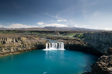 Scenic wide angle view of Thjofafoss waterfall and Hekla mountain on the background covered by snow